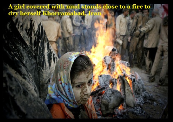 A girl covered with mud stands close to a fire to dry herself Khorramabad, Iran